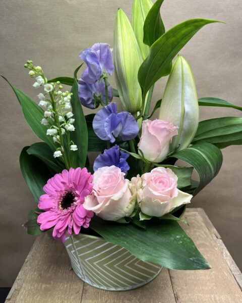 Composition Florale Muguet, Lys et Roses – Openflor Composition en pot vert rayé avec muguet, lys blancs, roses roses et pois de senteur, Openflor Lille.