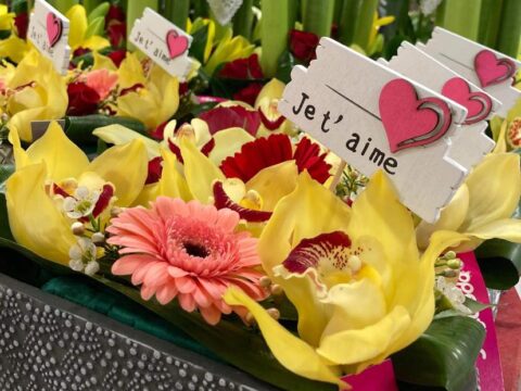 Composition florale « Aveu d’Amour » – Openflor Gros plan sur une composition avec orchidées Cymbidium jaunes, gerbera rose et panneau "Je t'aime", Openflor Lille.