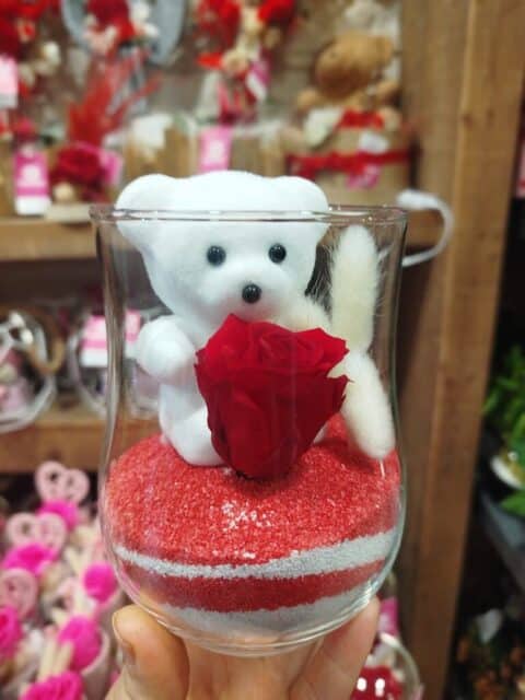 Rose Éternelle et Ourson sur Sable – Saint-Valentin Lille – Openflor Composition de Saint-Valentin avec rose éternelle rouge, ourson blanc et lagurus sur sable rouge et blanc - Openflor Lille.