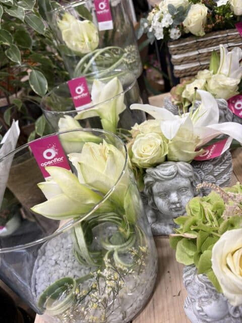 Compositions Amaryllis Blancs et Anges de Recueillement – Lille Vases en verre avec amaryllis blancs et statuettes d'anges en pierre garnies de roses blanches et hortensias, Openflor Lille.