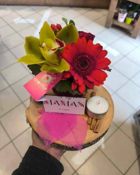 Composition sur rondin de bois – Orchidée et Gerbera Composition originale sur rondin de bois avec orchidée verte, gerbera rouge et bougie, Openflor.