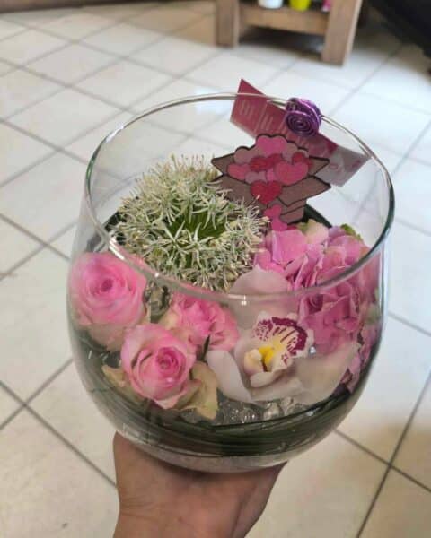 Composition en vase de verre – Orchidée blanche et roses Composition florale délicate dans un vase en verre avec orchidée blanche, roses et décoration cœurs, réseau Openflor.