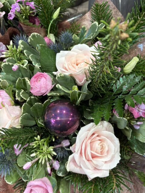 Bouquet de Noël douceur – Roses pâles et boule violette Bouquet de Noël aux teintes douces avec roses rose pâle, sapin et boule de Noël violette, fleuriste Openflor Lille.