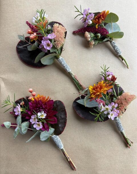 Boutonnières de mariage automnales – Dahlia et Wax Boutonnières de mariage aux couleurs d'automne avec petit dahlia bordeaux, fleurs de wax et ruban argenté, Openflor Lille.