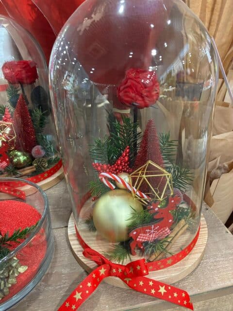 Cloche de Noël féérique – Rose éternelle rouge et décorations dorées Cloche en verre de Noël avec rose éternelle rouge, renne doré et décorations festives, artisan Openflor.