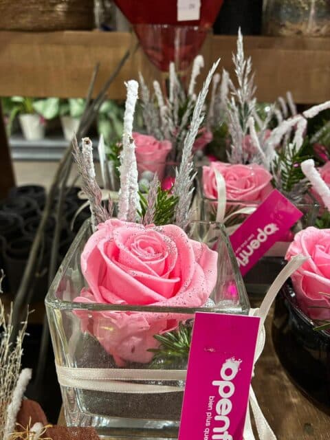 Composition de Noël en vase carré – Rose rose et neige Composition florale de Noël dans un vase carré en verre avec rose rose et branches enneigées, Openflor Lille.