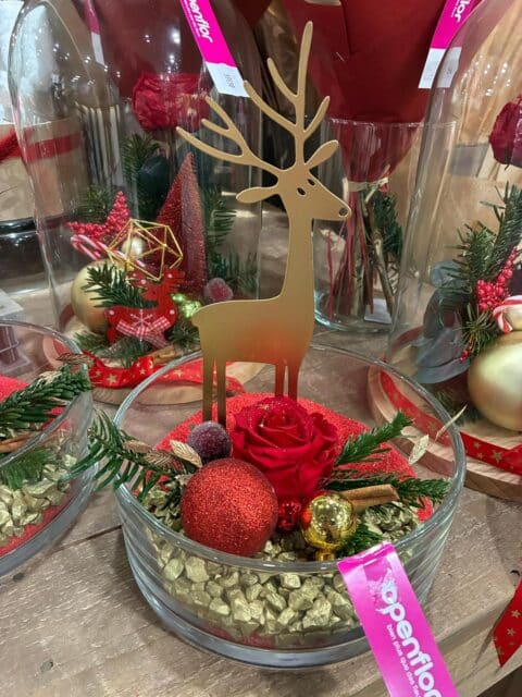 Coupe en verre féérique – Rose éternelle rouge et renne doré Coupe en verre de Noël avec rose éternelle rouge, gravier et silhouette de renne doré, Openflor Lille.