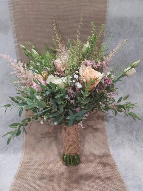 Bouquet de mariée champêtre – Roses pêche et astilbe Bouquet de mariée champêtre avec roses couleur pêche, astilbe rose et poignée en toile de jute, Openflor Lille.