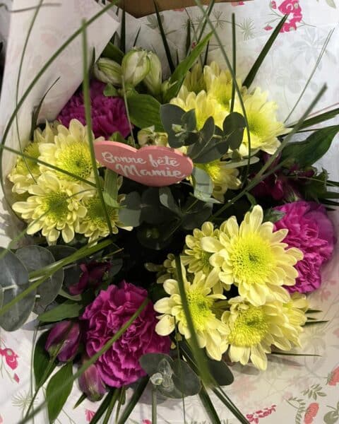 Bouquet chrysanthèmes jaunes et œillets violets – Cœur Bonne Fête Mamie Bouquet composé de chrysanthèmes jaunes lumineux et œillets violets avec un cœur Bonne Fête Mamie, fleuriste Openflor.