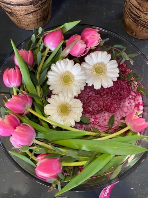 Centre de table design en coupe de verre – Tulipes et gerberas Centre de table floral original en coupe de verre avec tulipes roses, gerberas blancs et gravier décoratif, Openflor Lille.