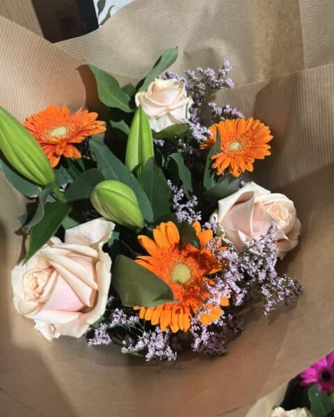 Bouquet chaleureux en emballage kraft – Roses, gerberas et lys Bouquet emballé dans du kraft avec roses pêche, gerberas oranges et lys, Openflor Lille.