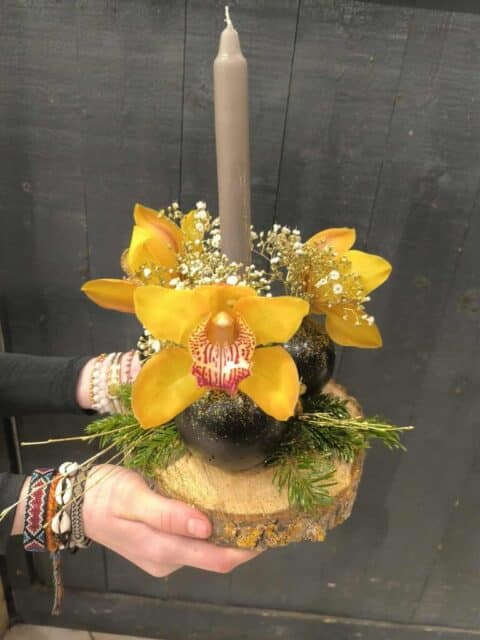 Centre de table sur rondin – Orchidées jaunes et bougie Centre de table de Noël sur rondin de bois avec orchidées cymbidium jaunes et bougie grise, fleuriste Openflor Lille.