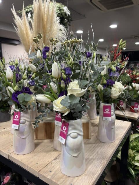 Vases de fêtes – Roses blanches et lisianthus violets Vases festifs en forme de visages avec roses blanches, lisianthus violets et branches argentées, Openflor Lille.